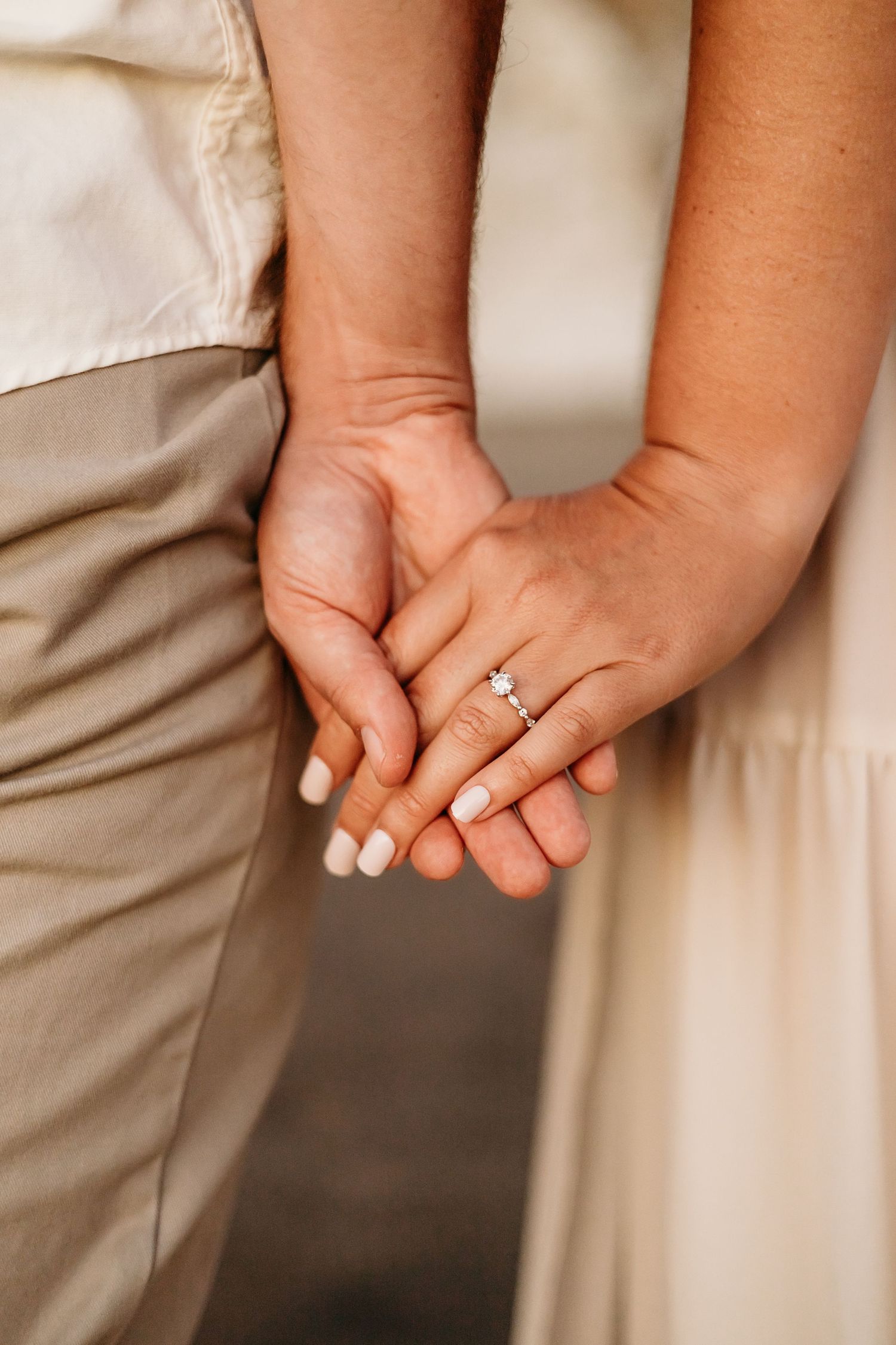 Close up of clasped hands showing an engagement ring against formal attire.