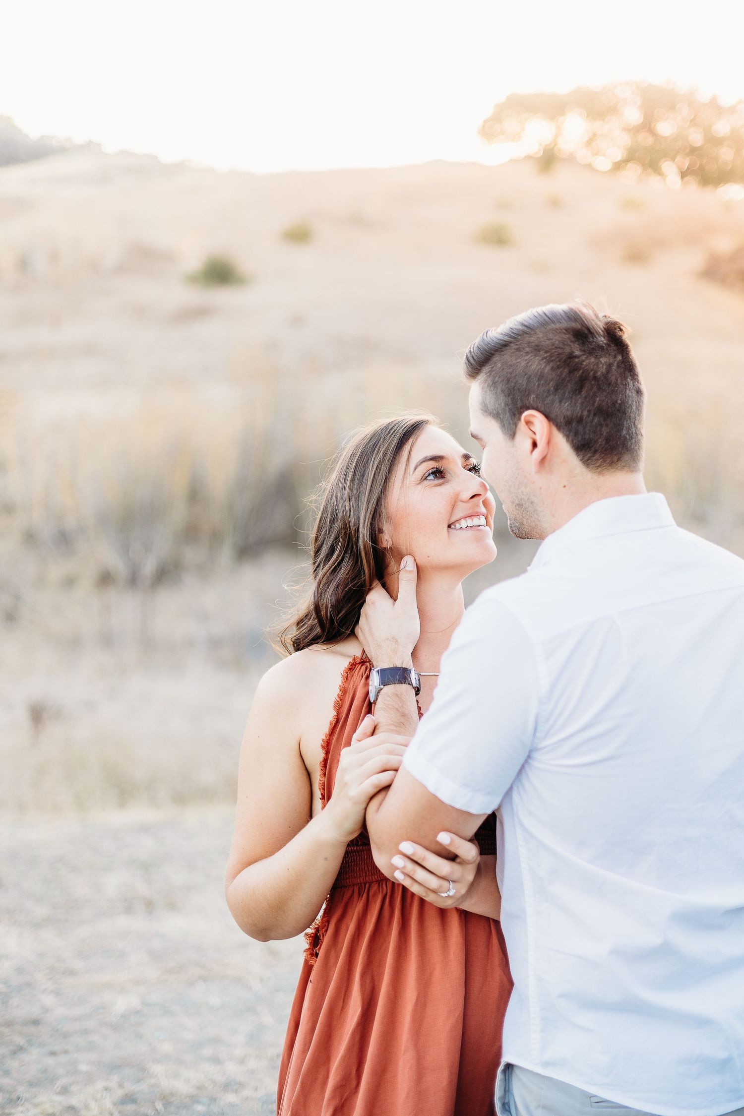 Joyful couple shares intimate moment against backdrop of sun-kissed hills.