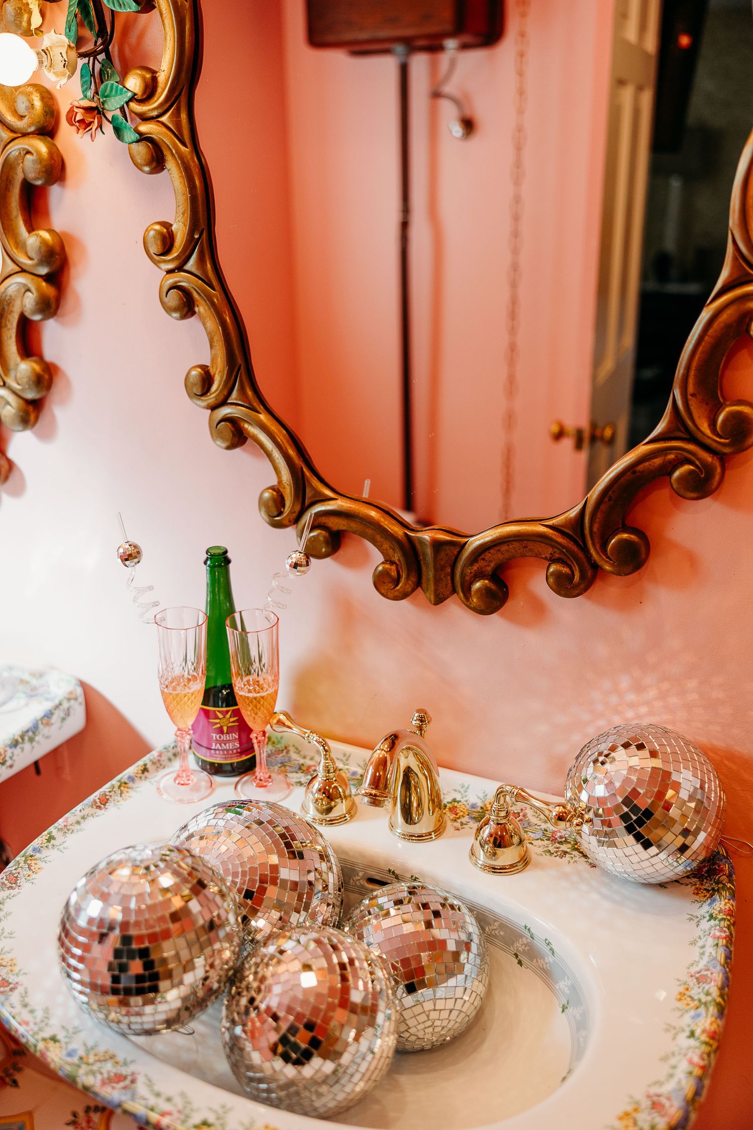 Disco balls and decorative items displayed on a pink surface with gold-framed mirrors.