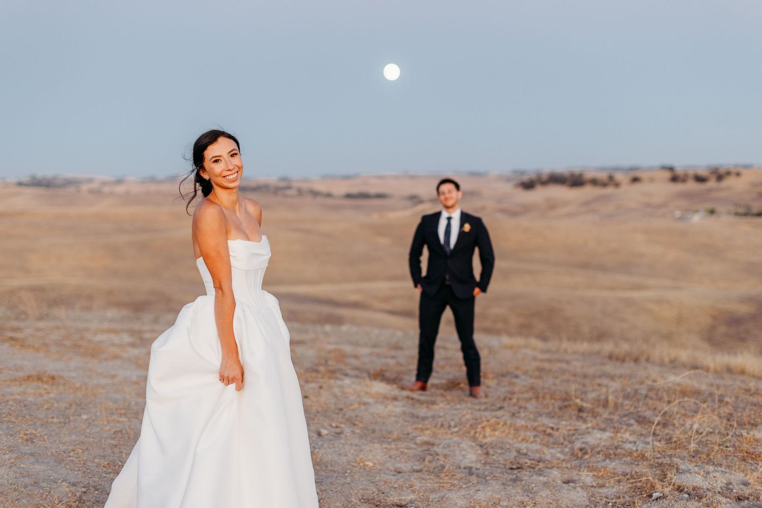 Wedding couple posing on a hilltop with dramatic desert landscape in the background.