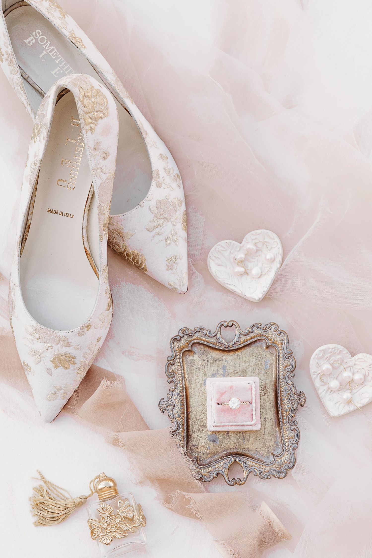 Delicate wedding accessories including white shoes and ornate frames on pink background.