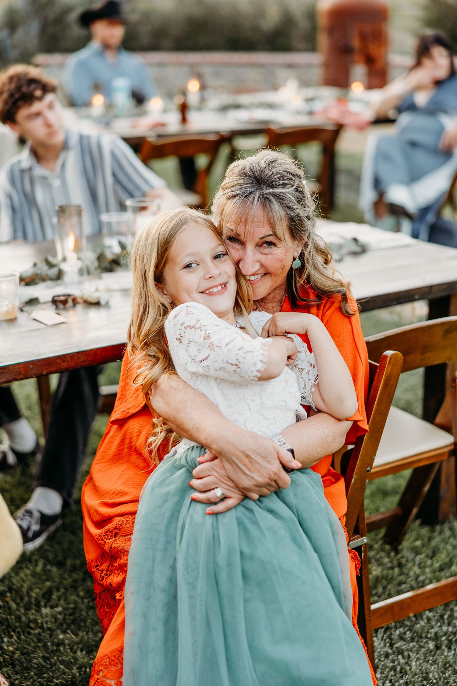 Candid moment between guests at outdoor reception with rustic wooden tables.