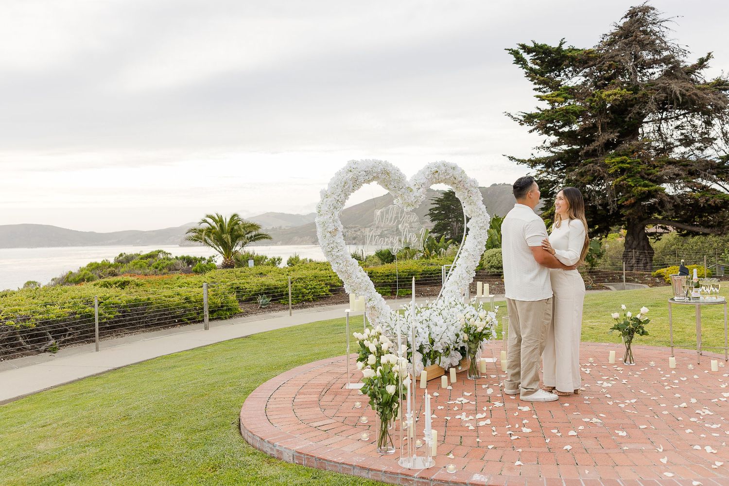 Guests gather on a grassy hillside overlooking the ocean for an outdoor wedding celebration.