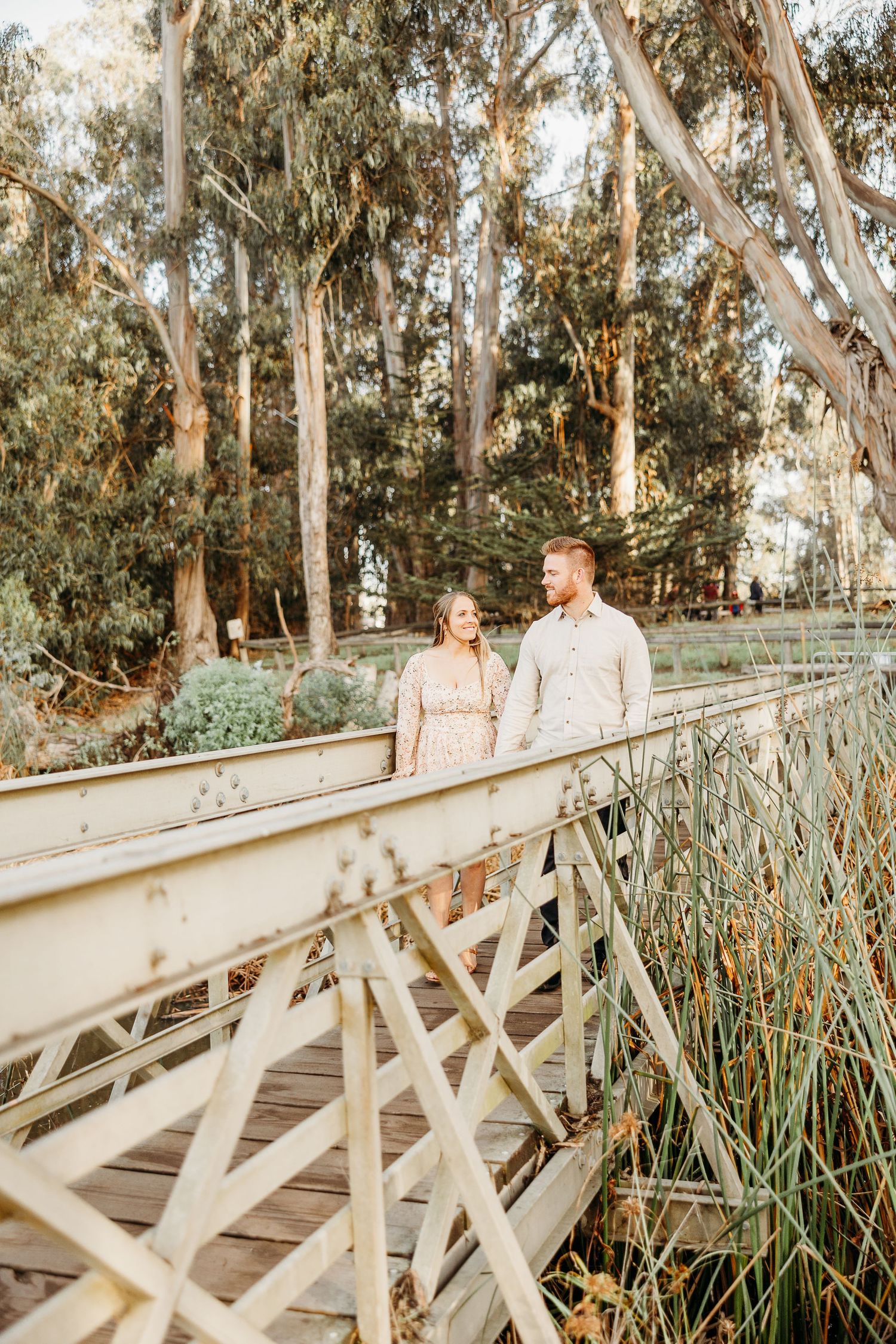 Couple standing on wooden bridge surrounded by tall eucalyptus trees at sunset.