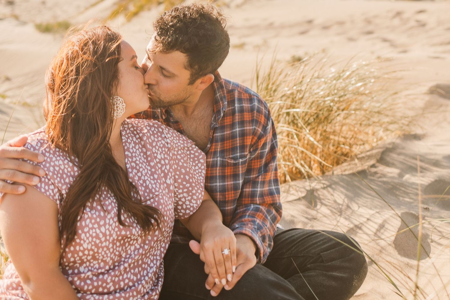 Intimate moment between couple sitting in beach dunes during golden hour.