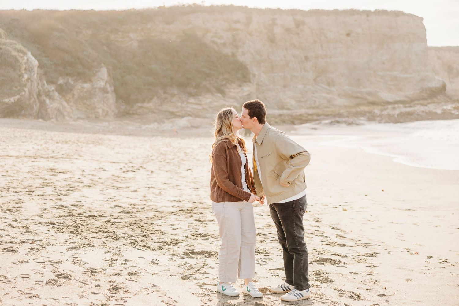 A romantic couple shares tender moments on a rocky beach during sunset.