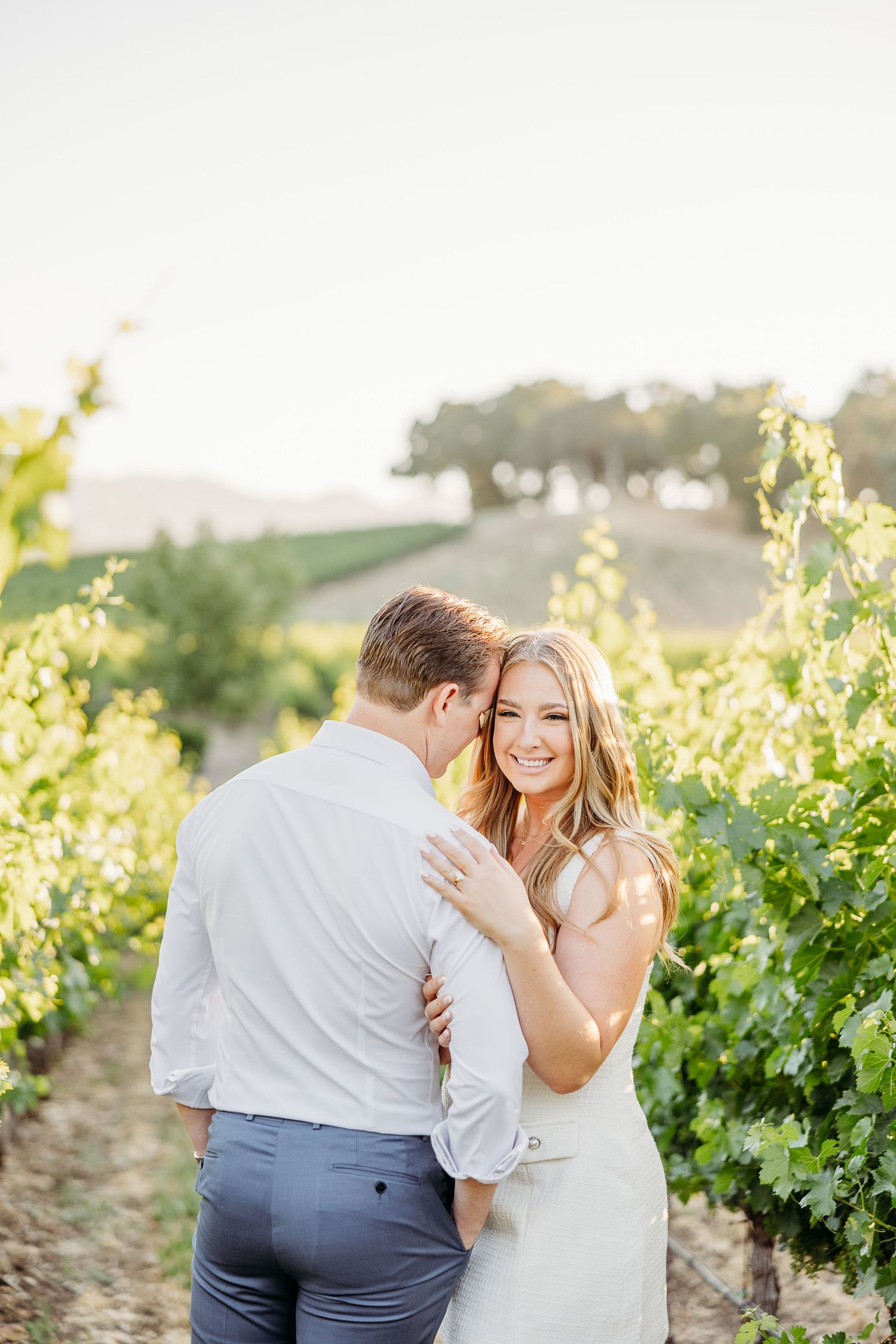 A romantic couple embraces in a sun-drenched vineyard during a golden hour photoshoot.