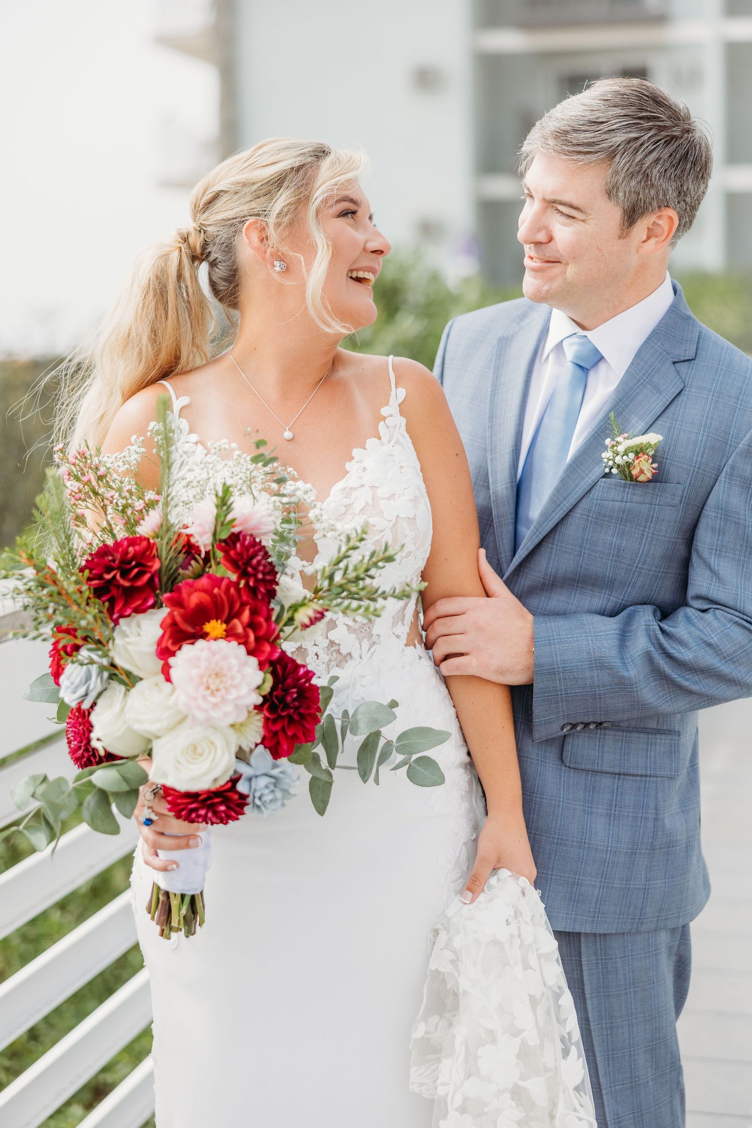 Happy couple in wedding attire posing on oceanfront balcony.