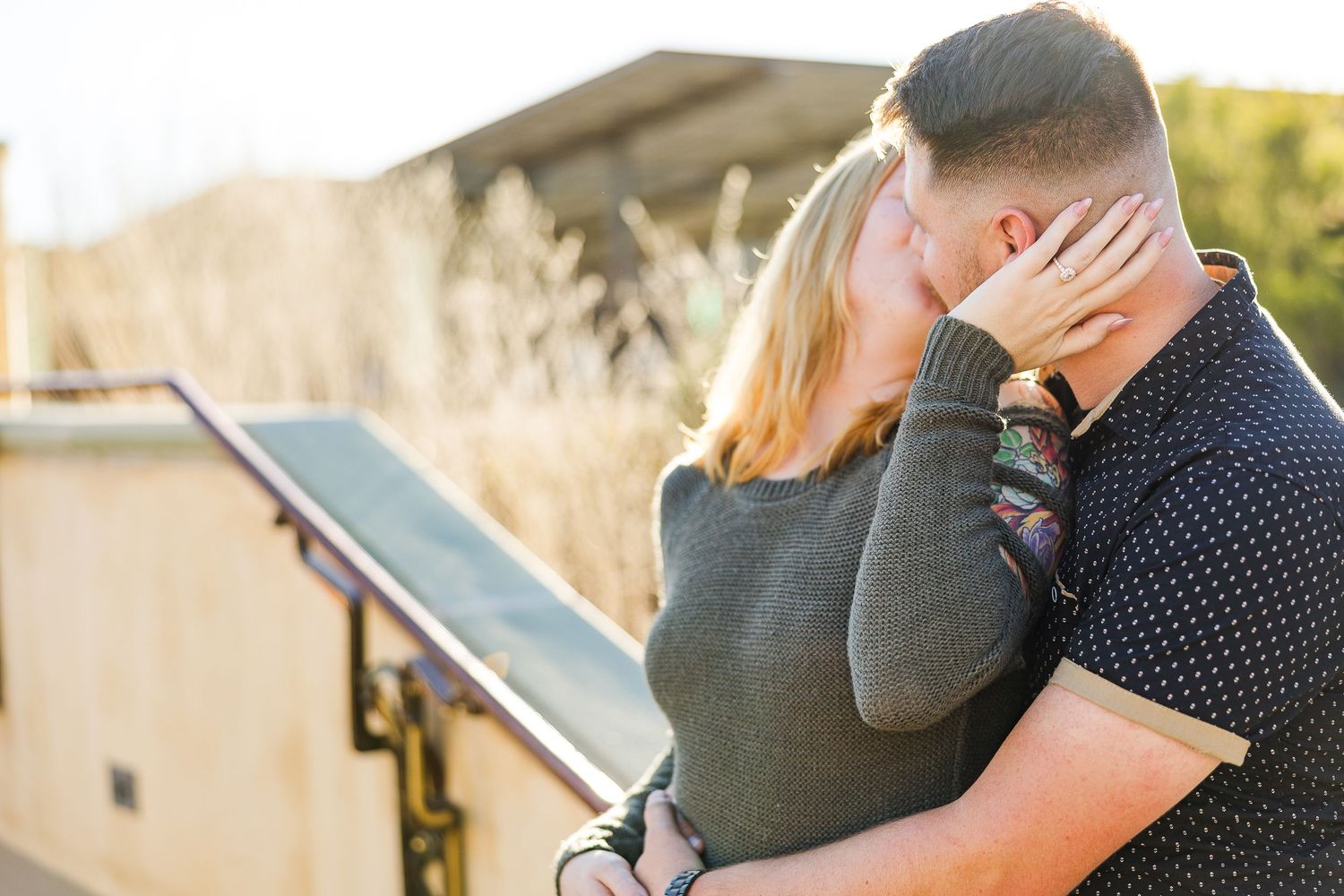 A couple shares a tender moment against a sunlit outdoor backdrop.