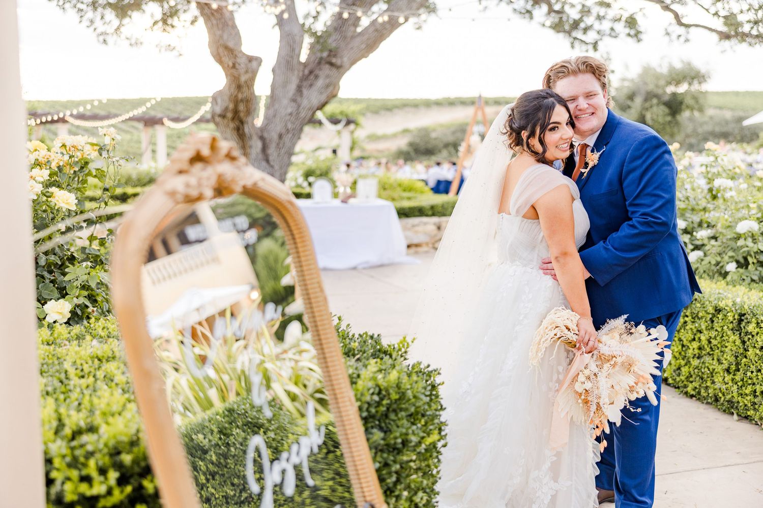 A romantic wedding moment captured next to a decorative mirror in a garden setting.