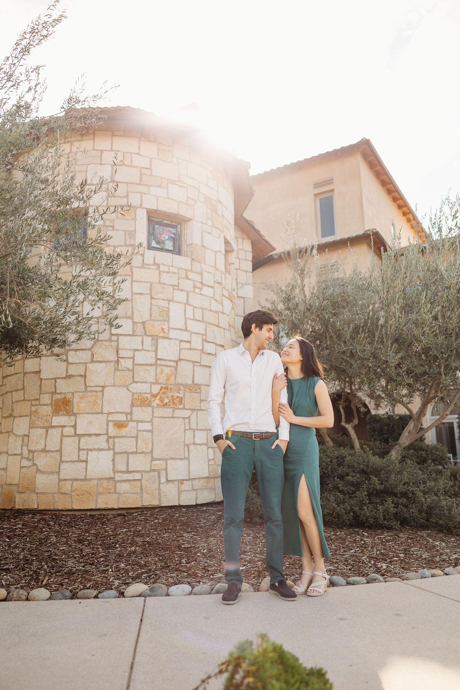 A couple sharing a romantic moment together outside a Mediterranean-style stone building with olive trees.