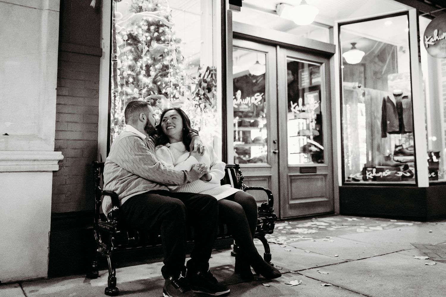 Black and white photo series showing two people walking past illuminated storefronts at night.
