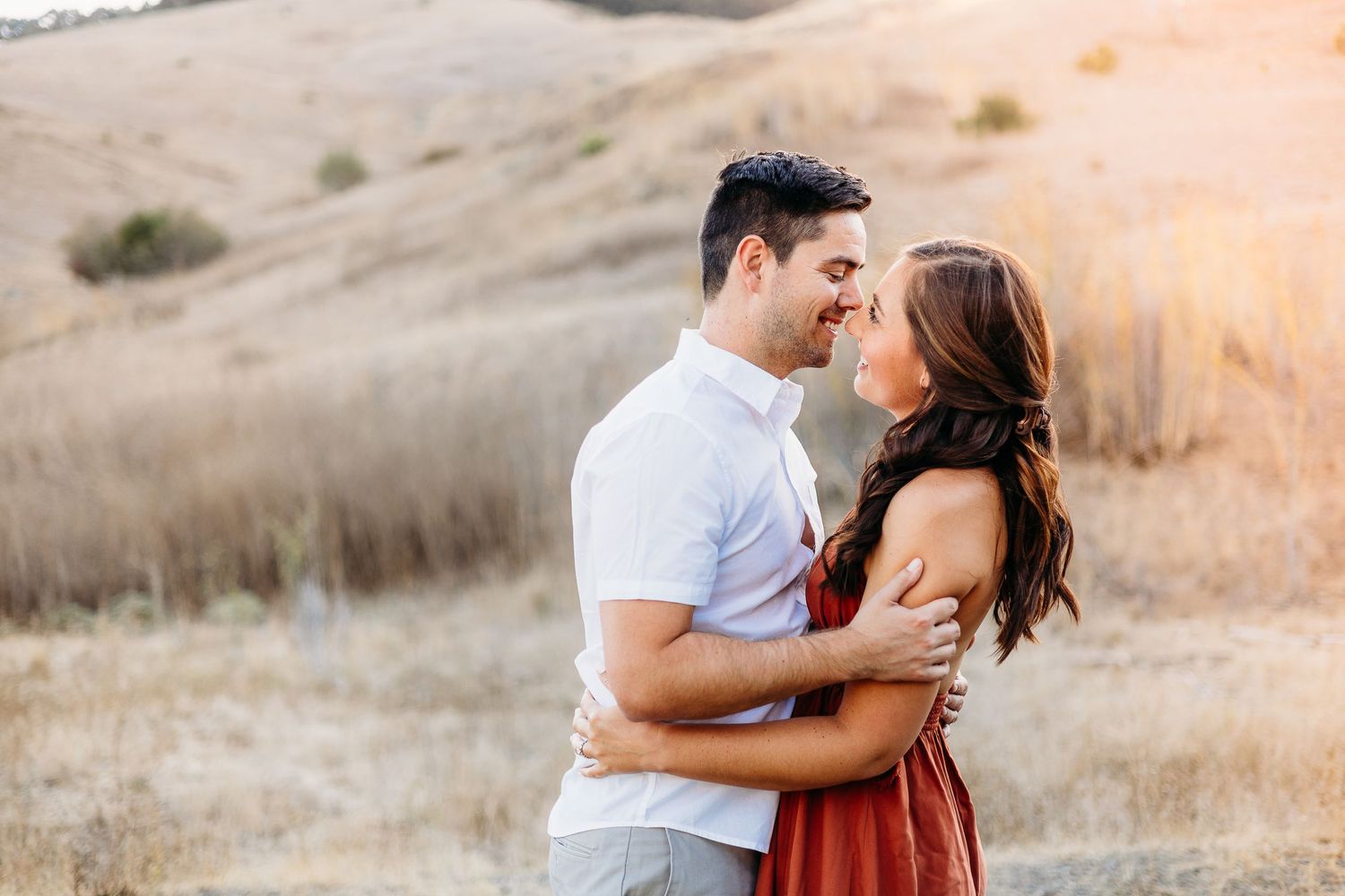 Couple shares a tender moment while standing on a hill during sunset.
