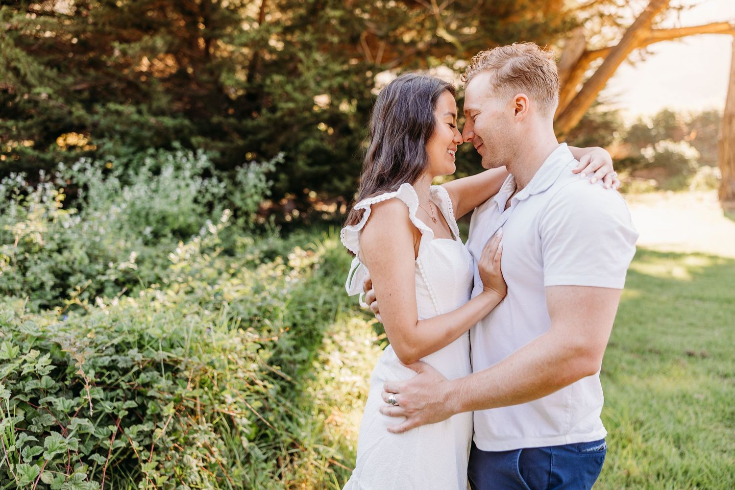 Romantic couple embracing in golden sunlit garden setting wearing white and casual attire.