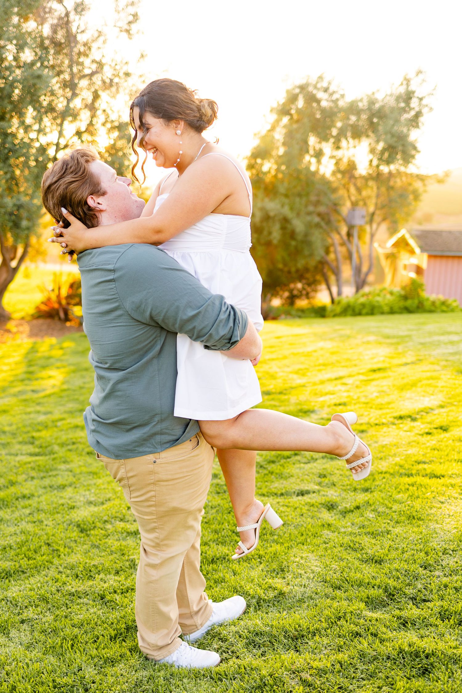 Joyful couple shares romantic lift pose on green lawn during sunset.
