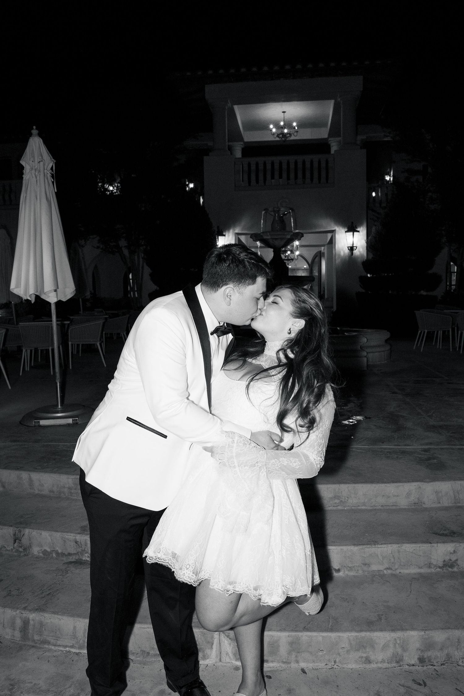 Black and white photo of bride and groom sharing a kiss outdoors at night after wedding.