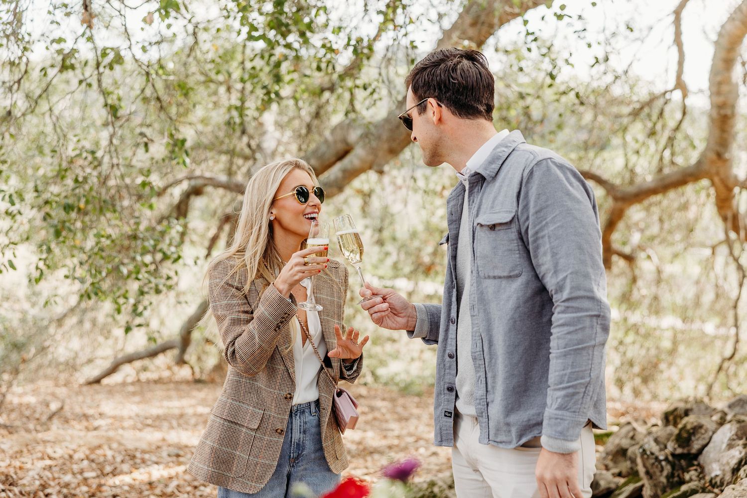 Couple enjoying a romantic moment together in a sunlit forest with oak trees in the background.