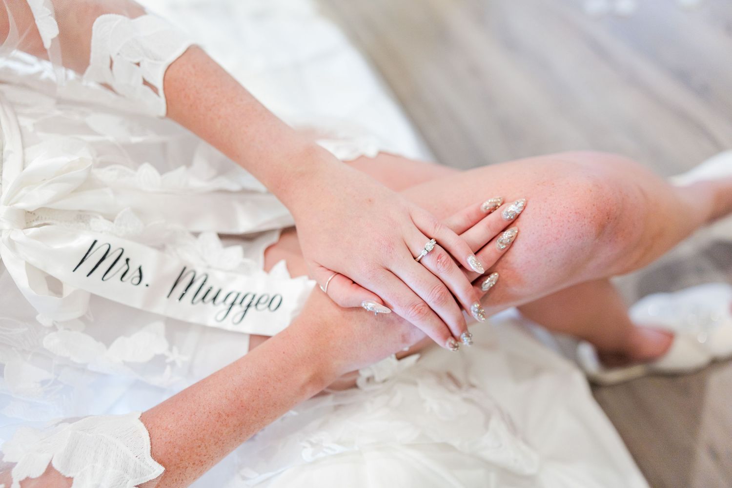 Close-up of hands showing wedding ring with 'Mrs' text visible on white lace fabric.
