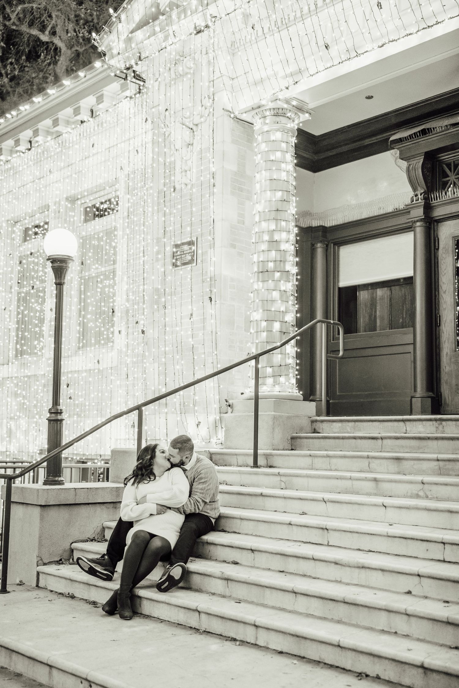 Black and white photo series showing a couple sitting and embracing on outdoor stone steps of a brick building.
