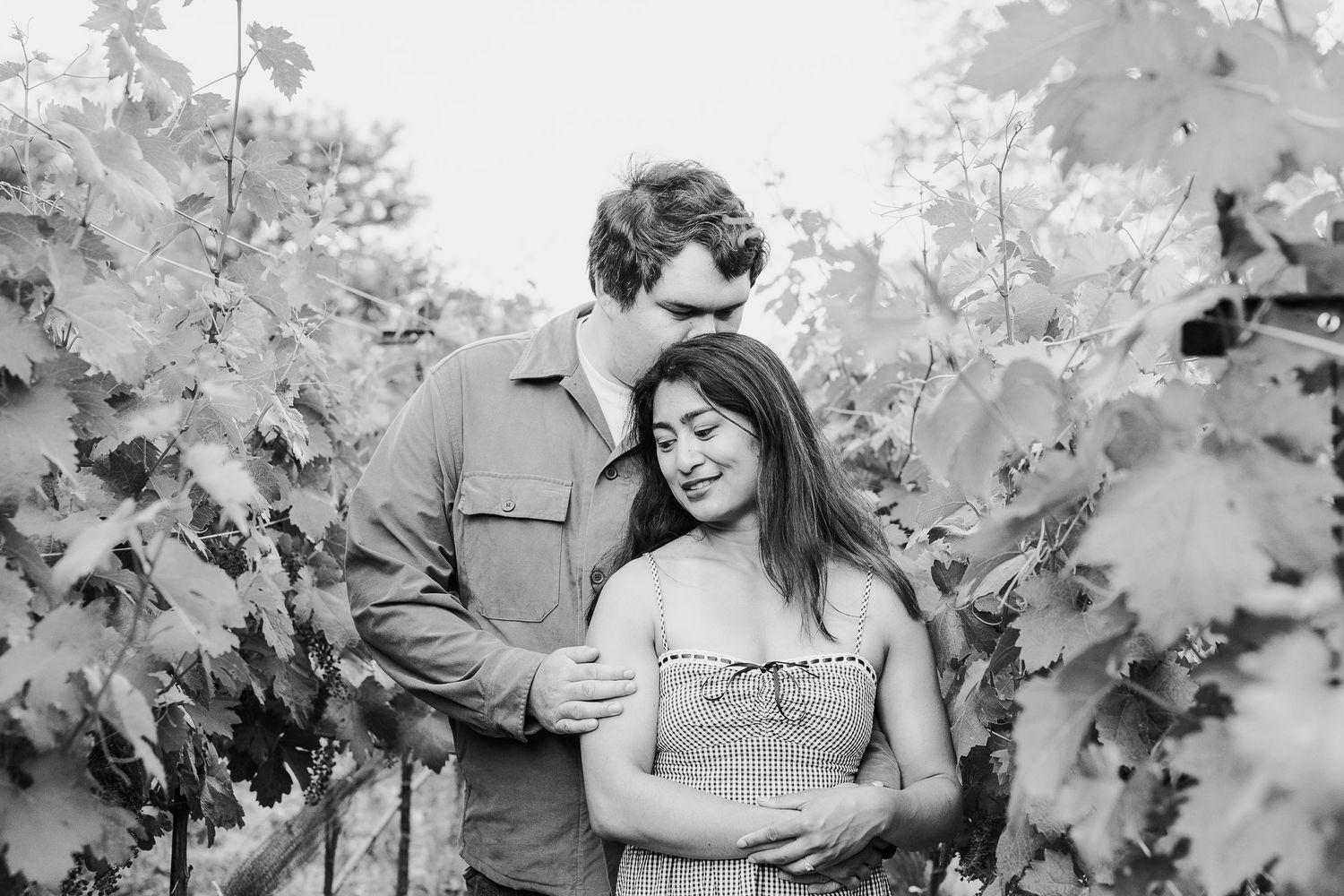 Black and white photo series showing intimate moments between a couple among vineyard rows during an engagement session.