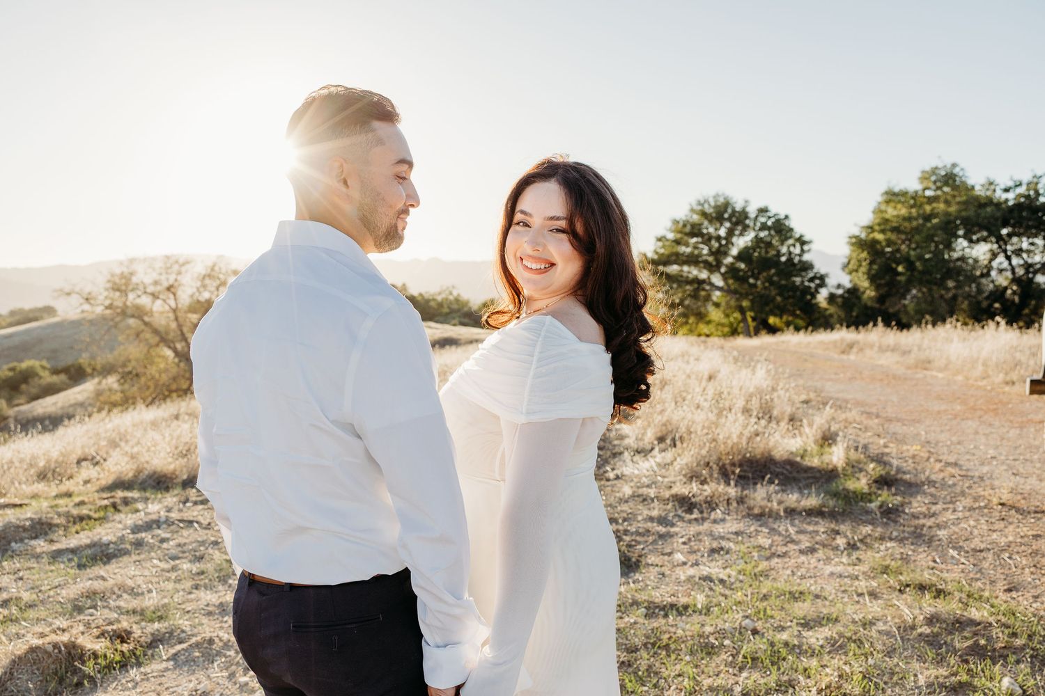 A couple dances and embraces on a golden hillside during sunset.