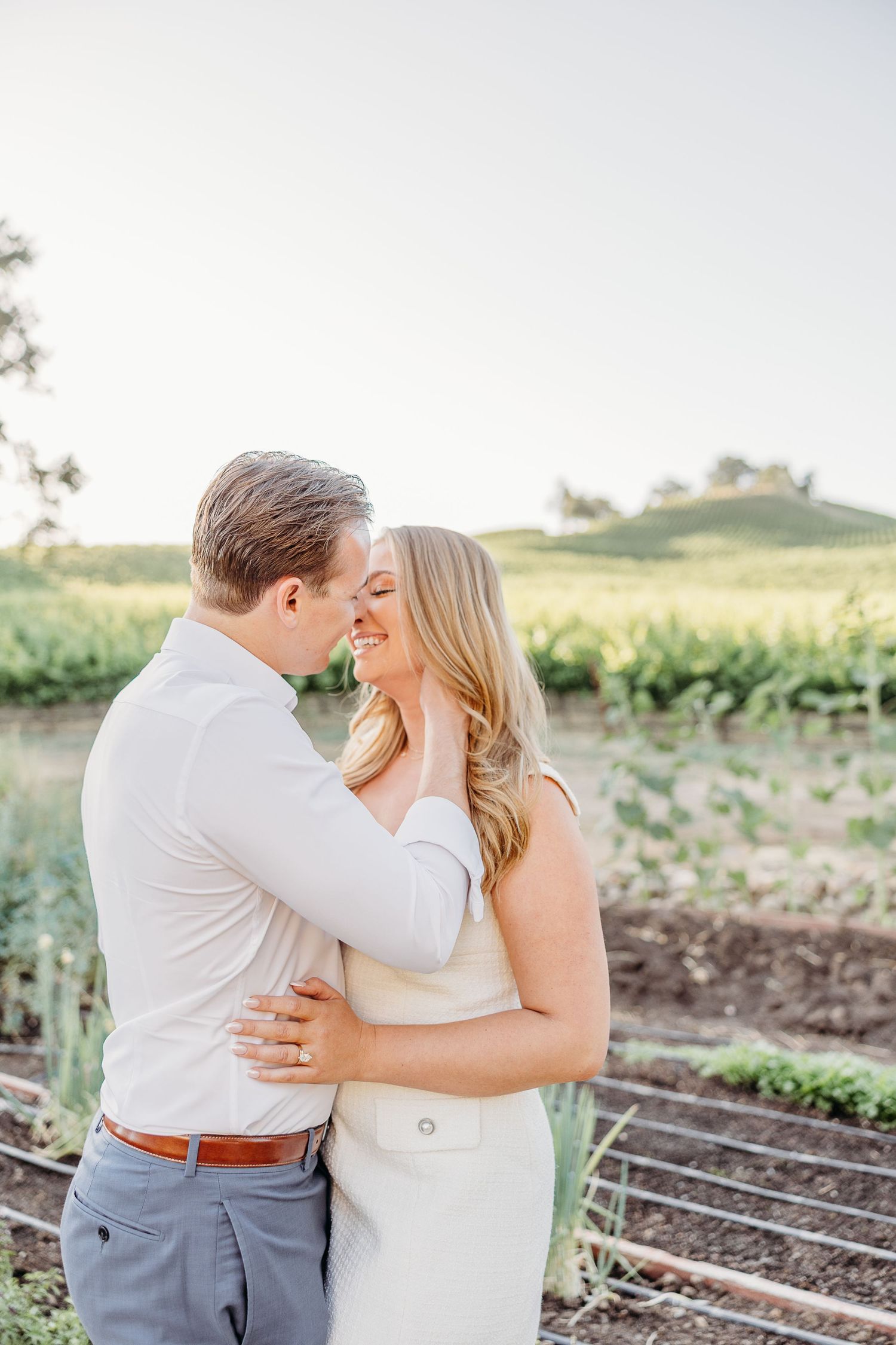 A couple embraces in a romantic moment together in an outdoor garden setting at sunset.