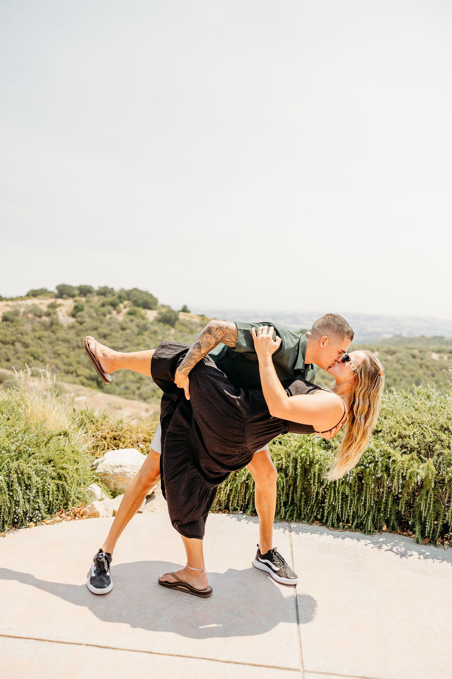 A person in a black dress performs a dynamic dance sequence on a hilltop path with mountains in the background.