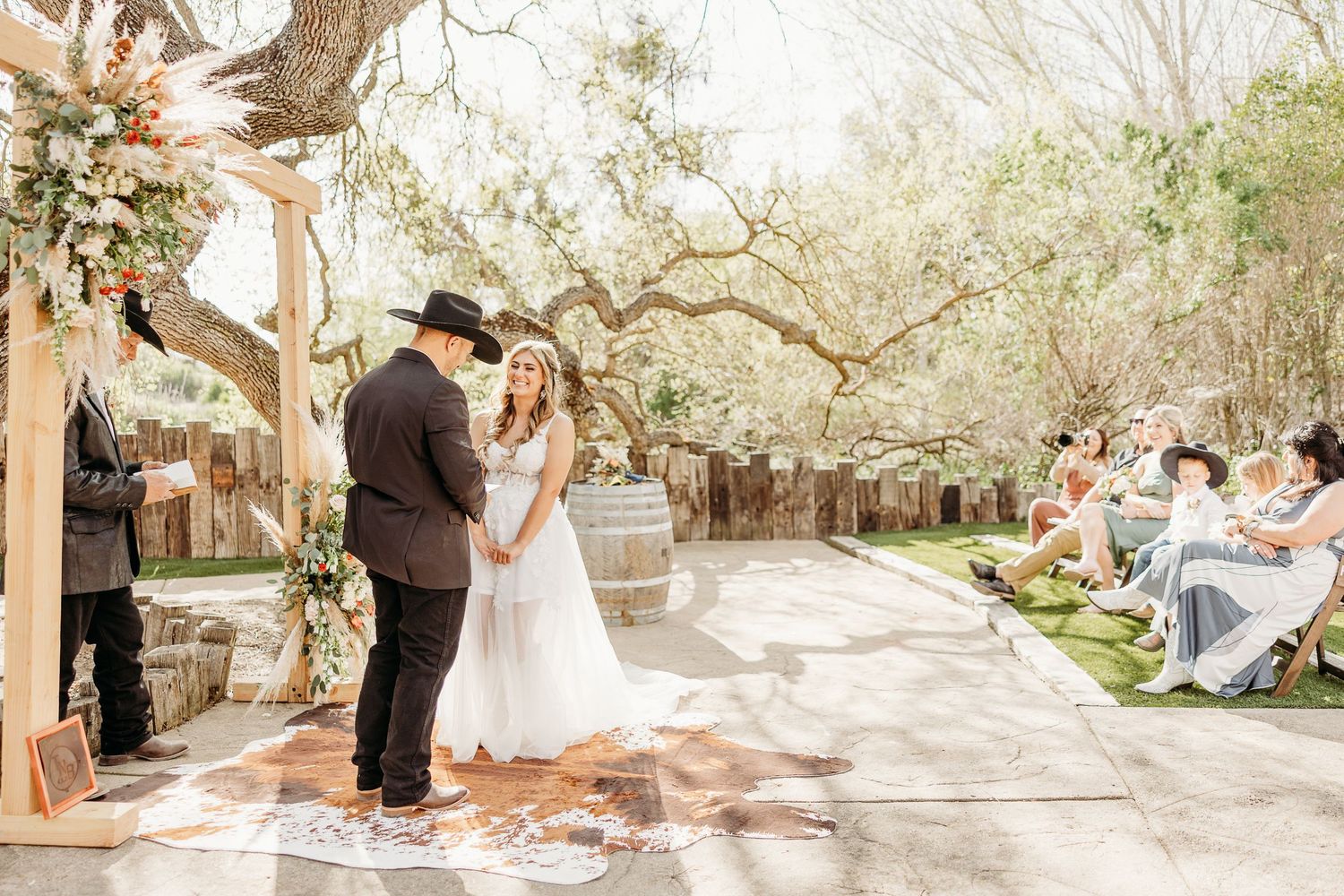 A couple exchanges vows during an intimate outdoor wedding ceremony with guests seated on wooden benches.