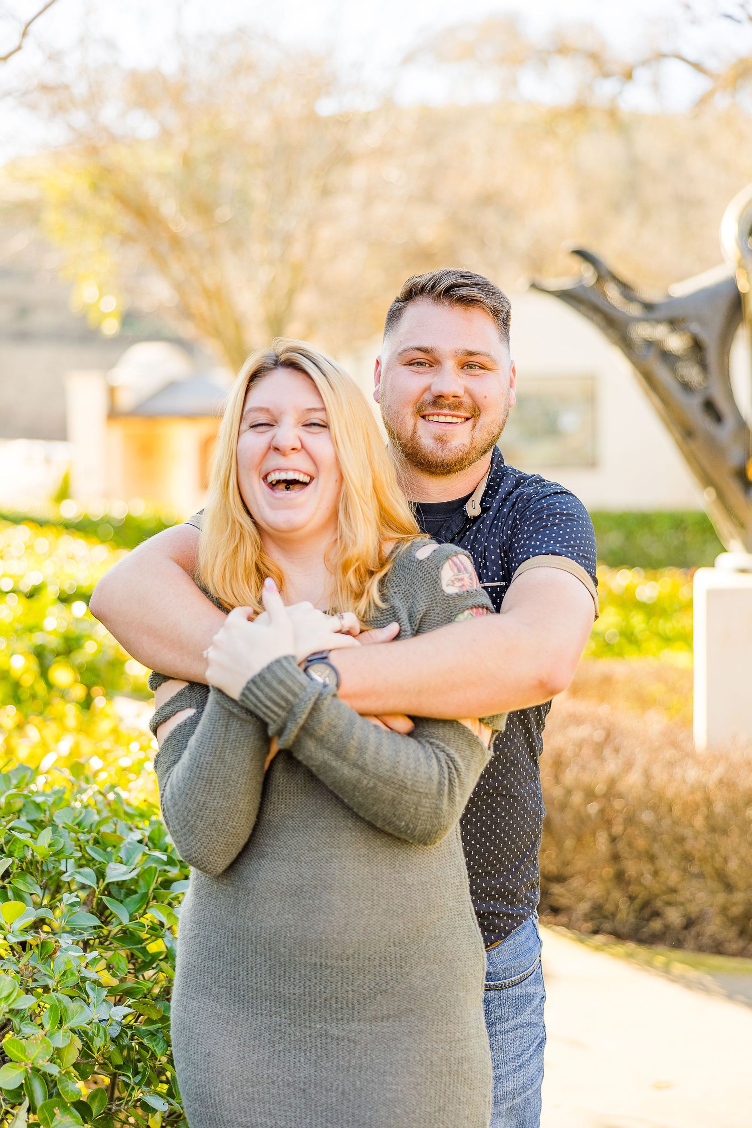 Joyful moment captured as couple laughs together in a sunny outdoor garden setting.