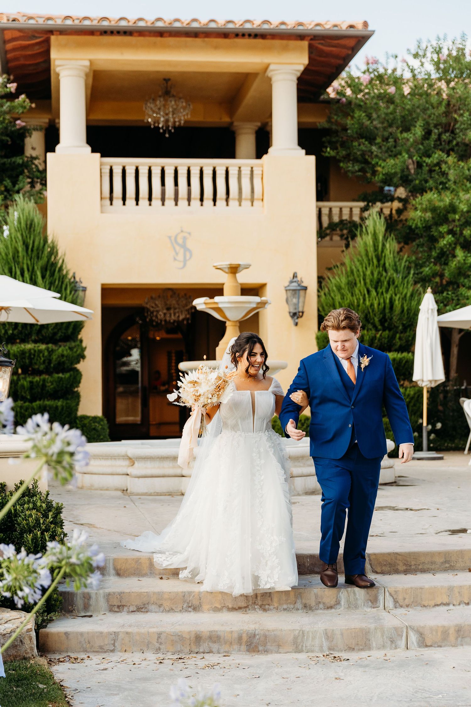 Wedding celebration at Mediterranean villa with stone steps and tiered fountain in foreground.
