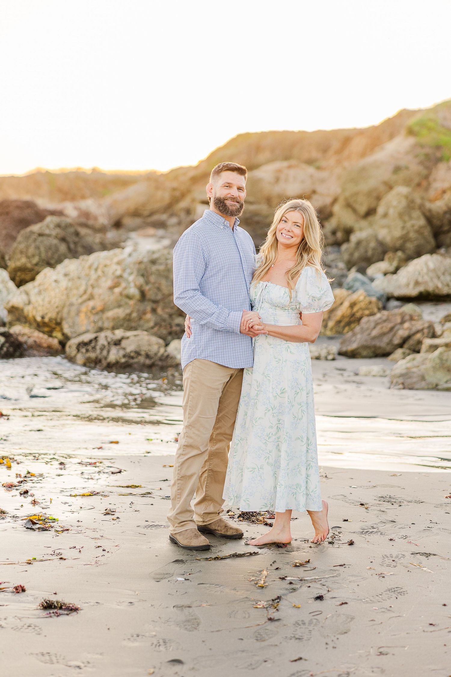 A couple shares a romantic moment on a rocky beach during golden hour.