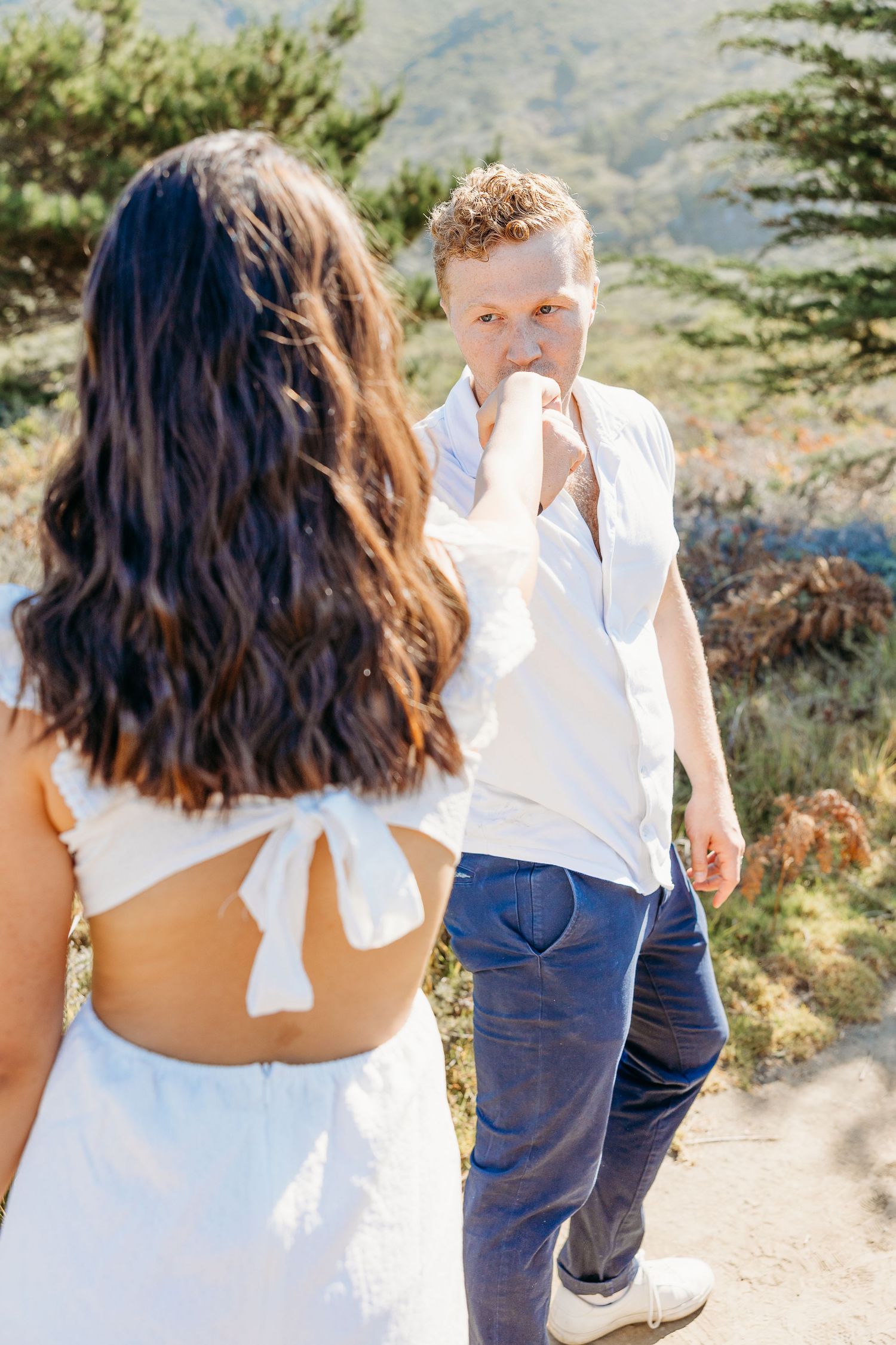 Couple shares intimate moment on mountain trail surrounded by coastal vegetation.