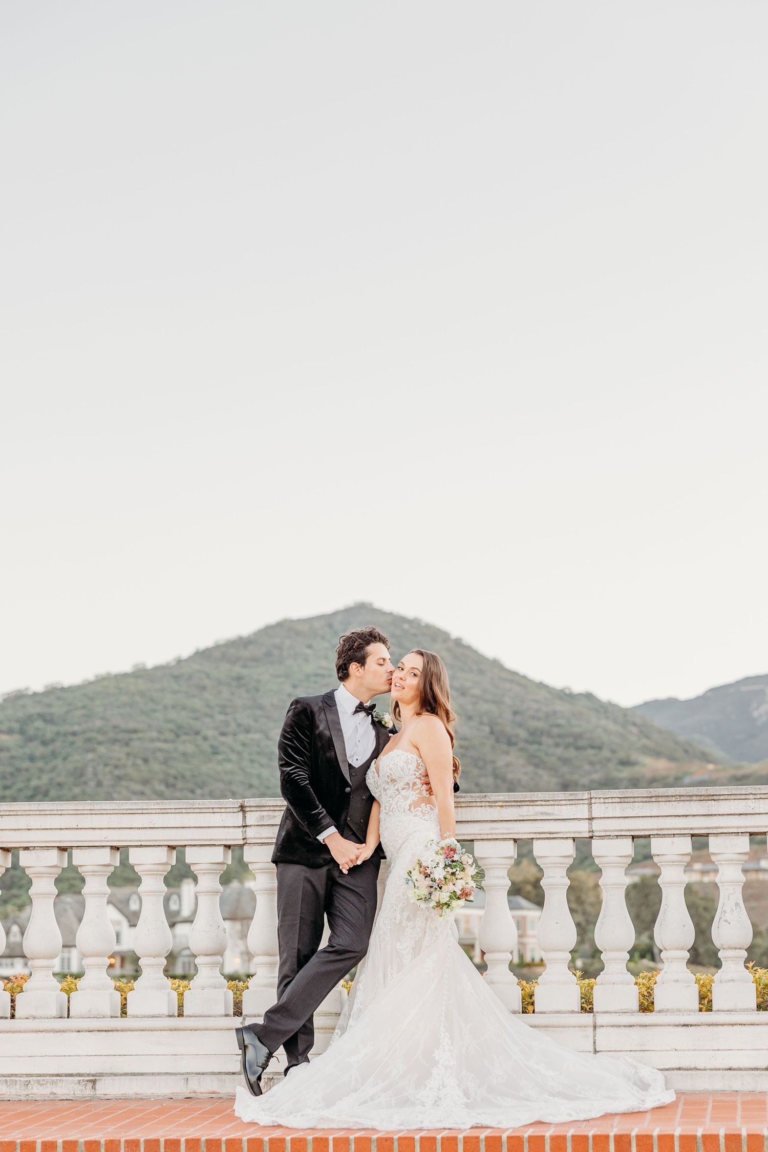 Romantic wedding portrait on an elegant balcony overlooking mountain scenery.