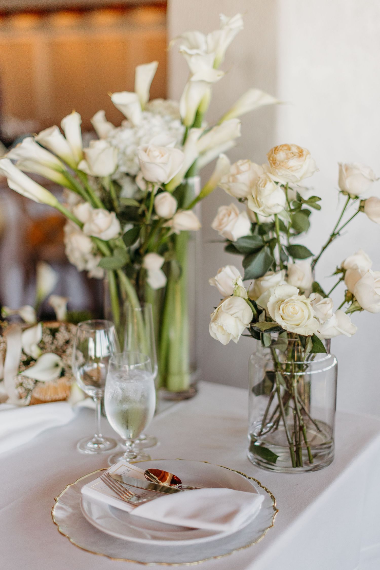 Elegant white floral centerpieces in glass vases line a wedding reception table with place settings.