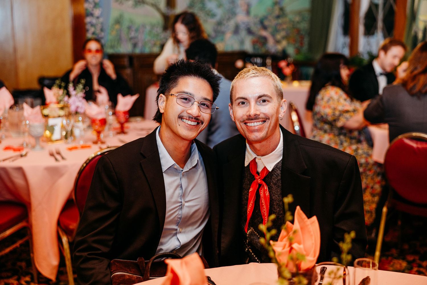 Wedding reception guests enjoying themselves at decorated indoor venue with warm lighting.