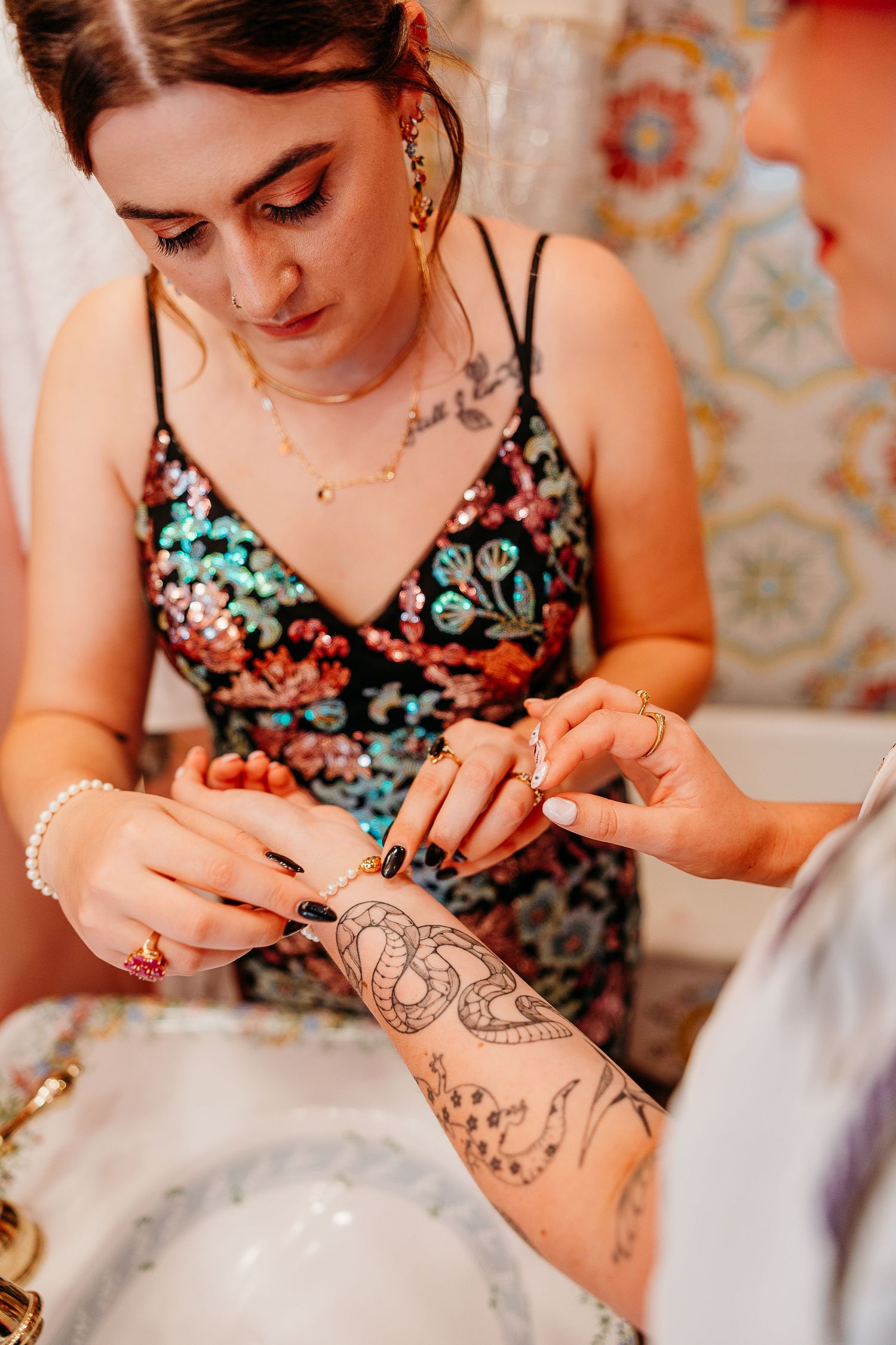 Person in floral dress drawing henna designs on another's arm.