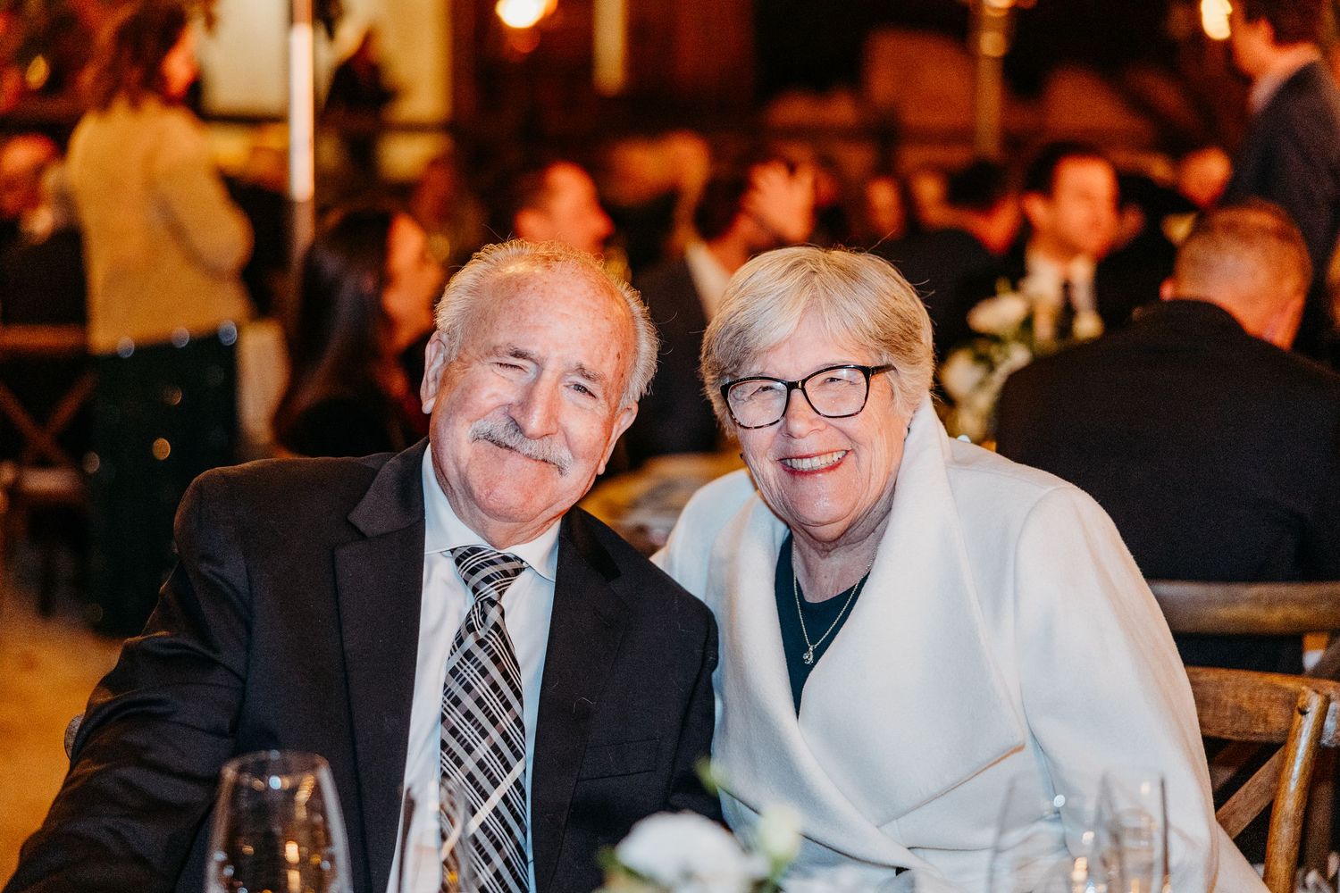 Wedding reception guests enjoy evening celebrations at tables with warm lighting.