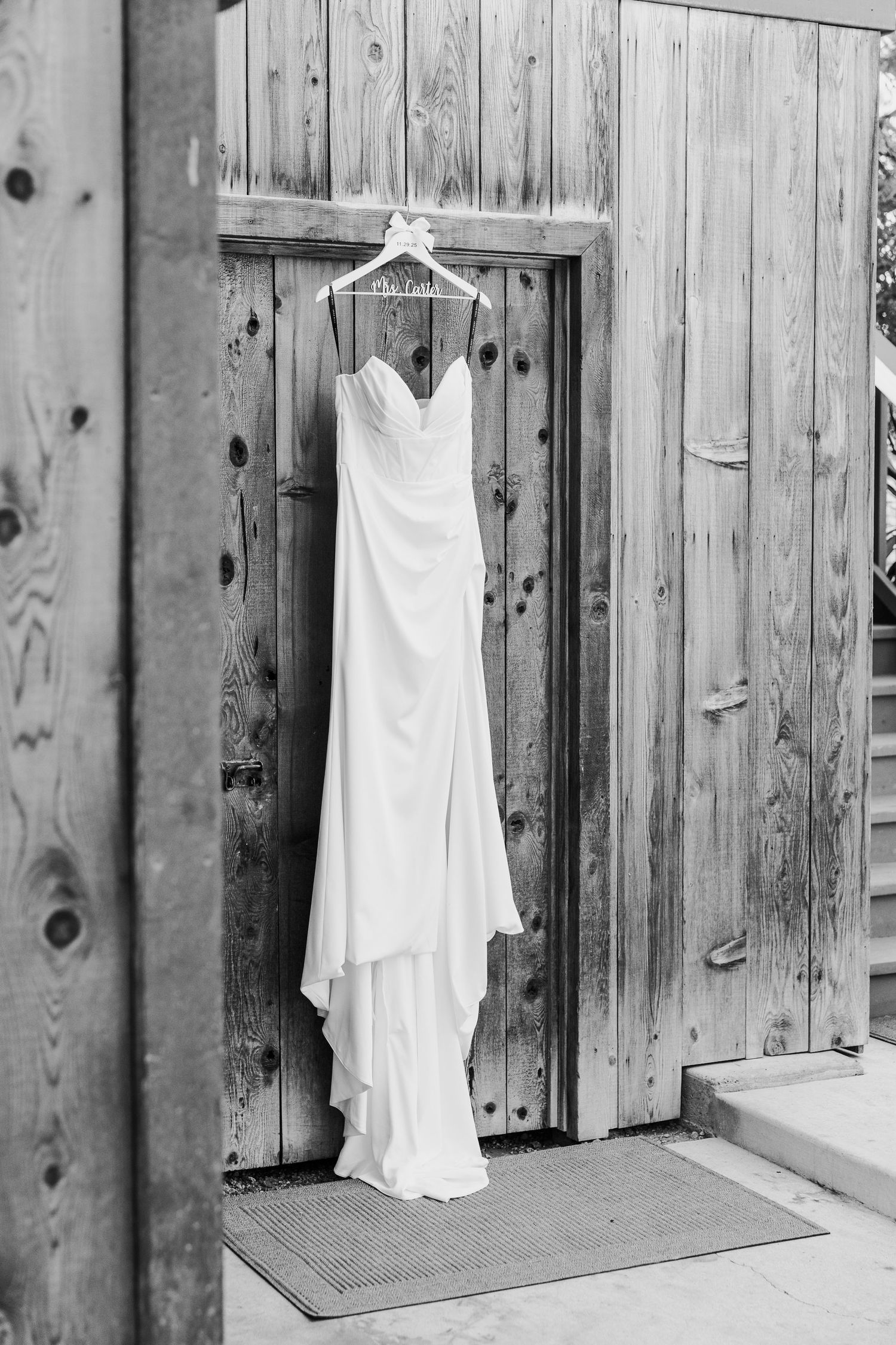 A sequence of white wedding dresses hanging on rustic wooden doors in black and white.