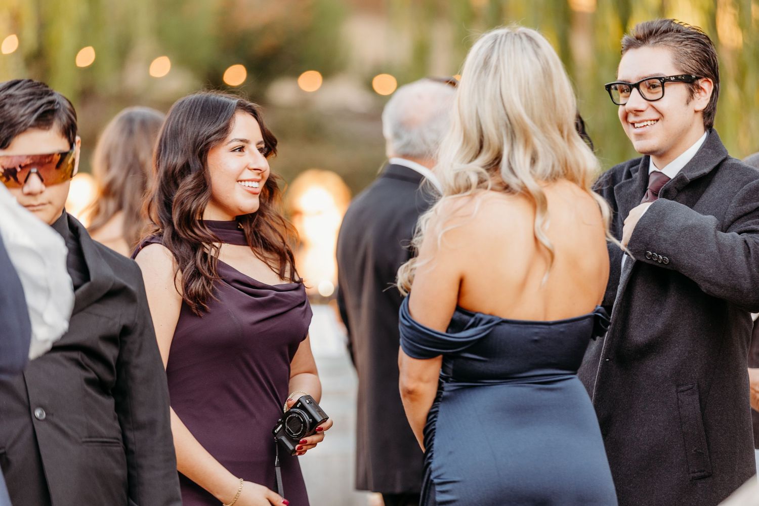 Wedding guests dance together on a dimly lit dance floor with bokeh lights in the background.