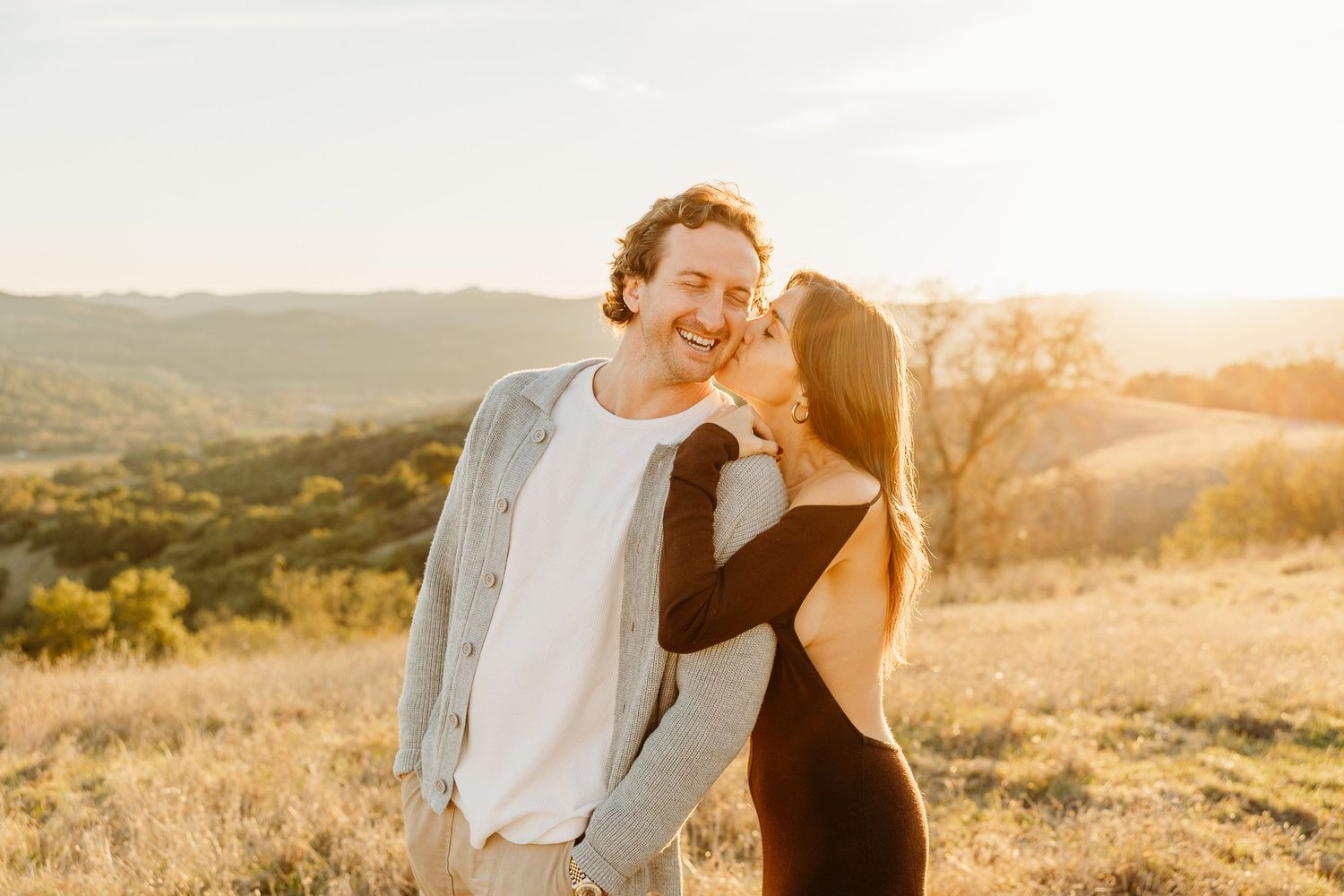 Couple sharing a tender moment on a sunlit hillside during a golden hour photoshoot.
