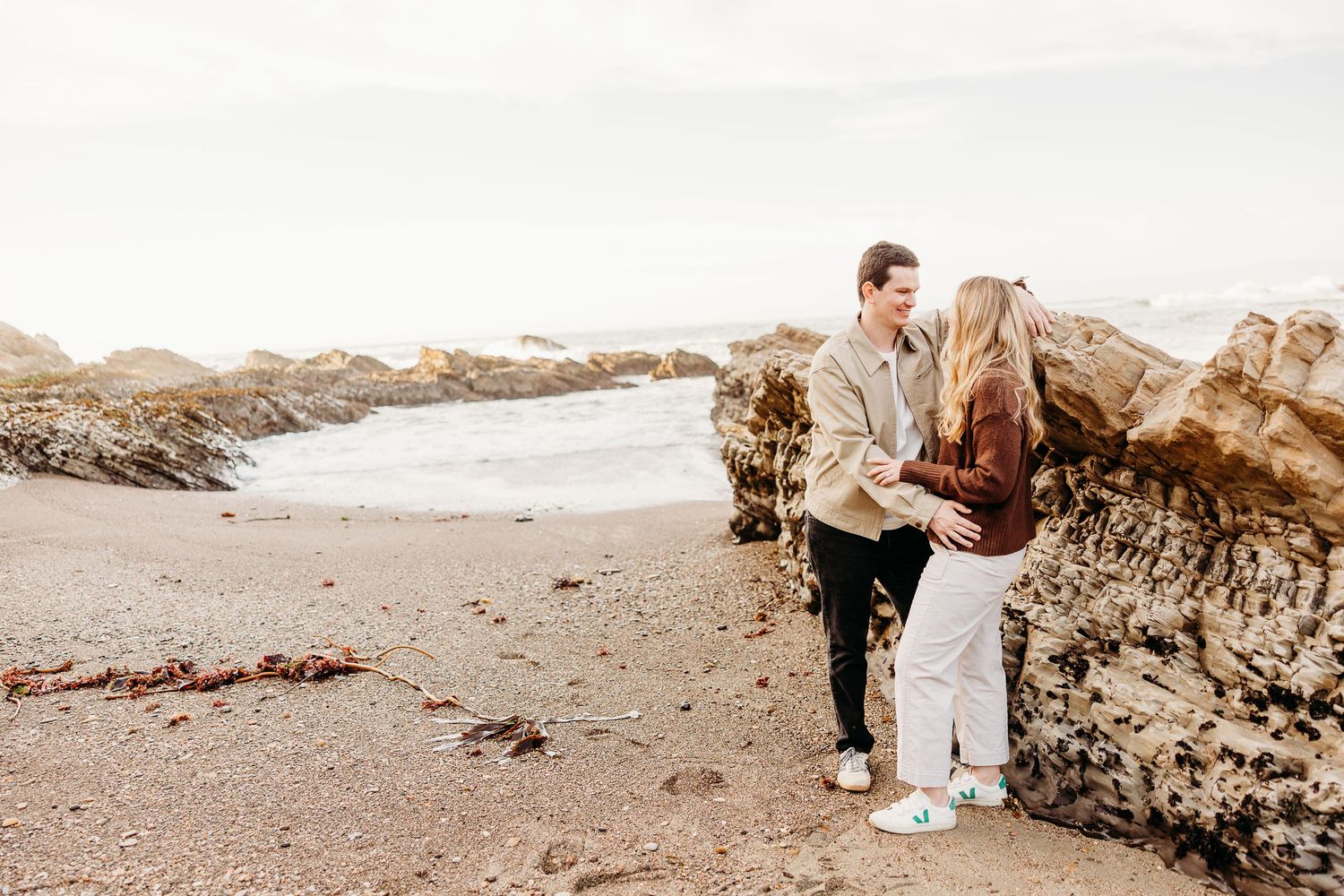 A romantic beach engagement photoshoot at sunset with rocky cliffs in the background.