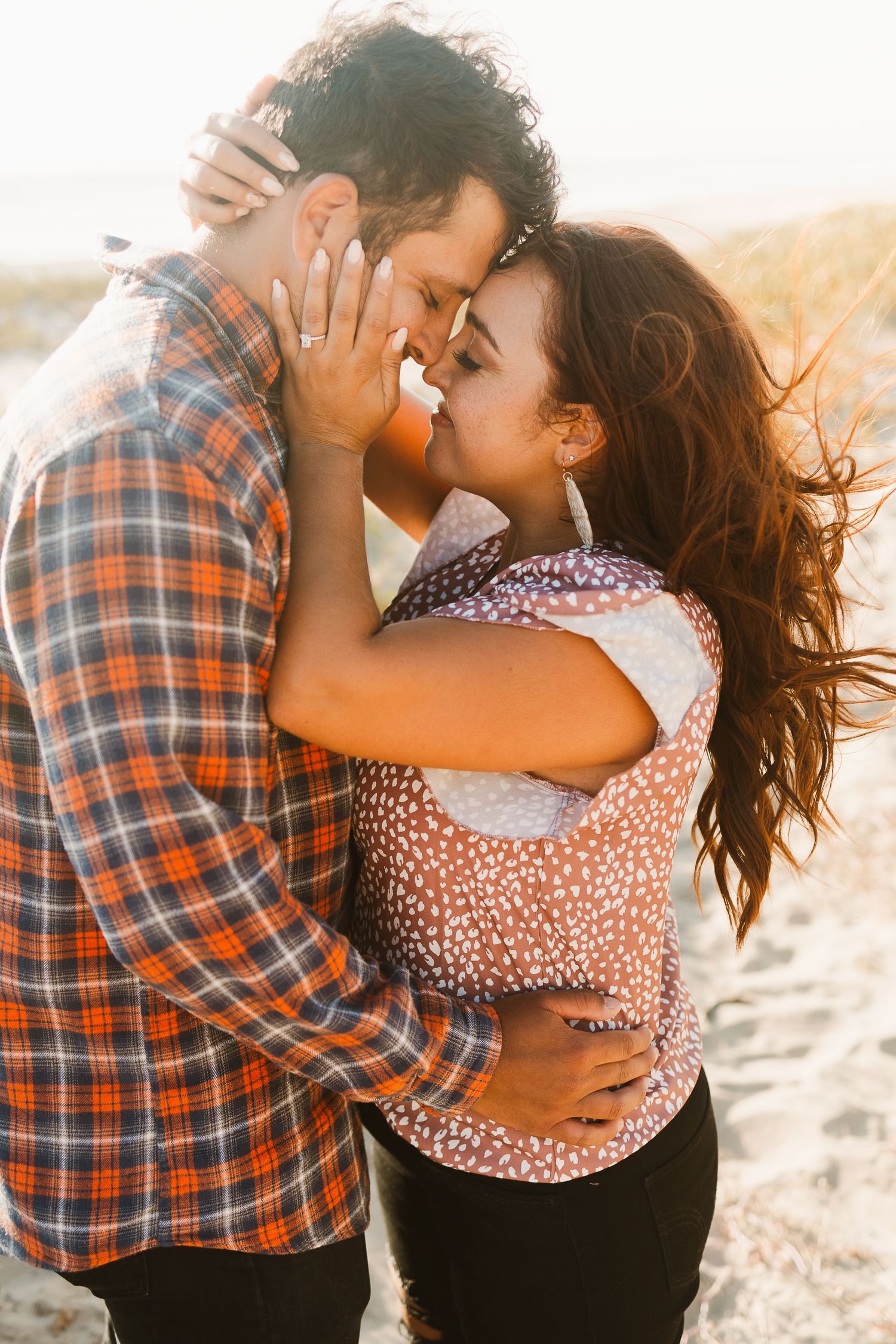 Couple sharing romantic moment on beach with sunlit backdrop.