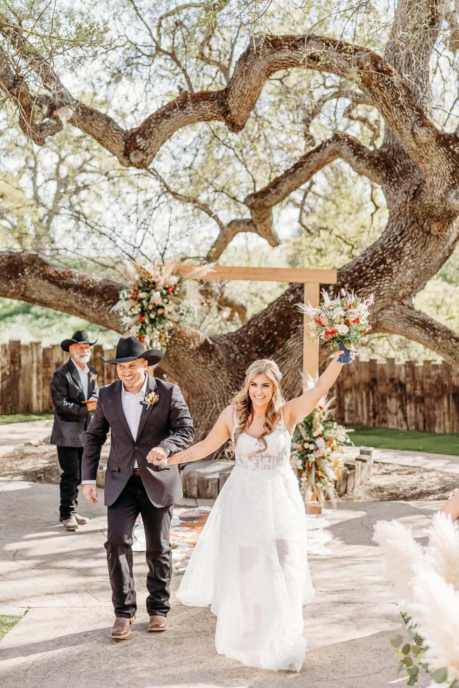 A couple celebrates under a uniquely curved heart-shaped tree during their rustic outdoor wedding ceremony.