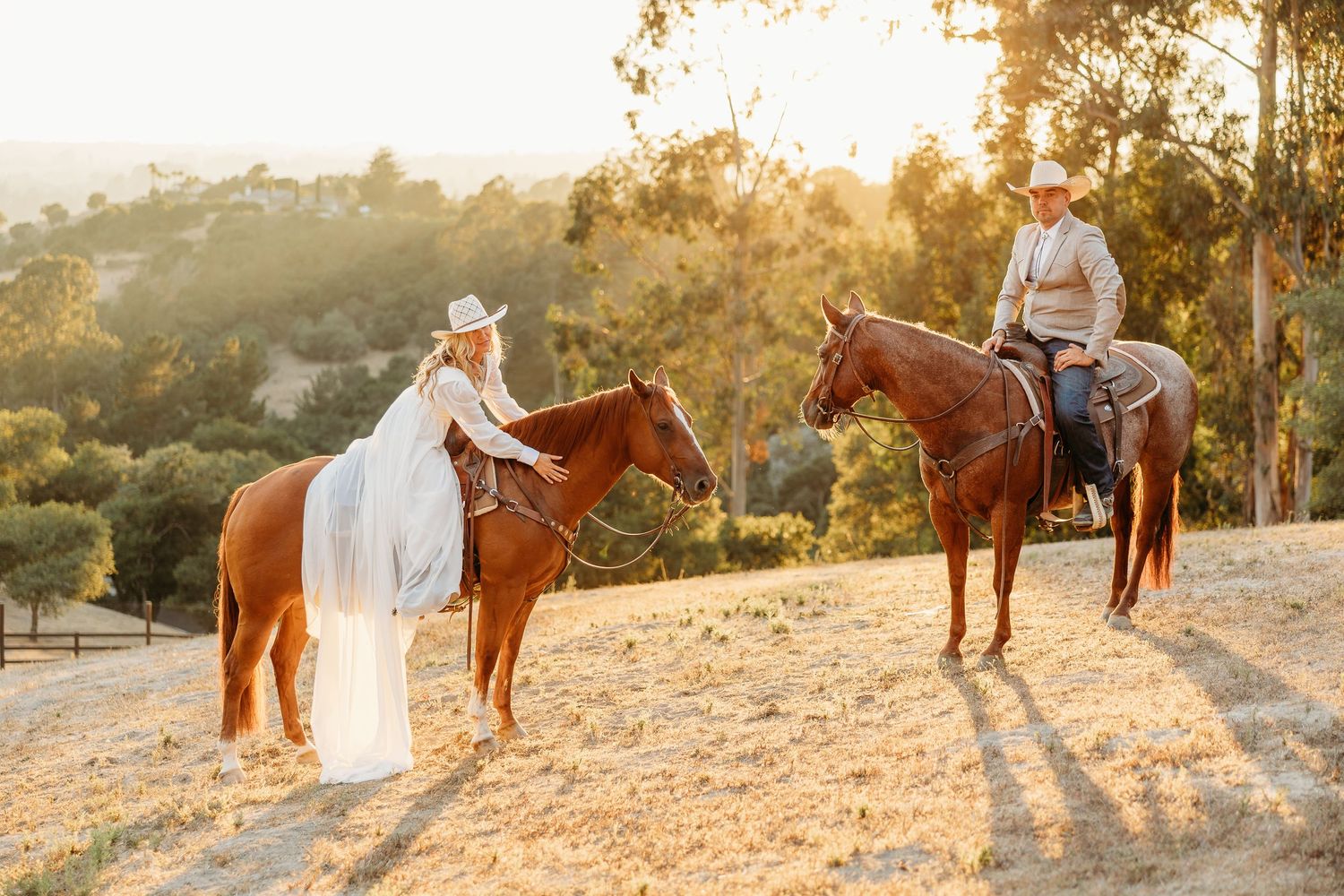 Two riders on horses at sunset in a golden-lit mountainous landscape.