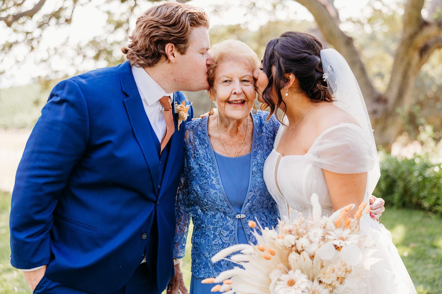 Sweet moment shared between couple and elderly relative in blue dress at outdoor wedding.