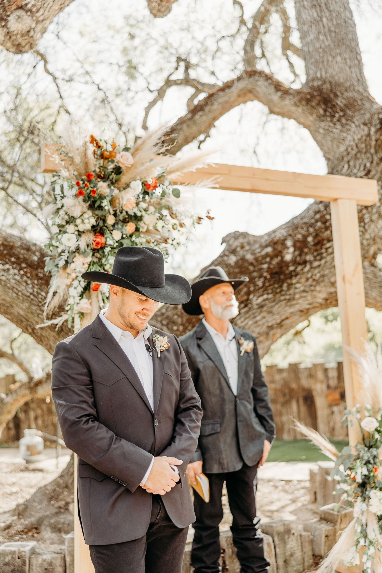 Groomsmen in dark suits and cowboy hats stand under a floral-decorated wedding arch.