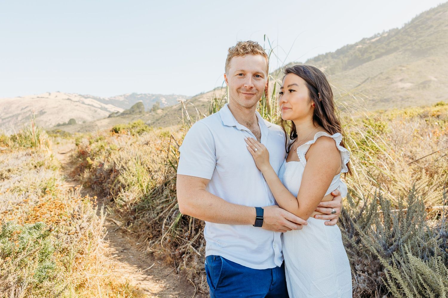 Romantic couple in coordinating outfits share a tender moment on a hillside trail.