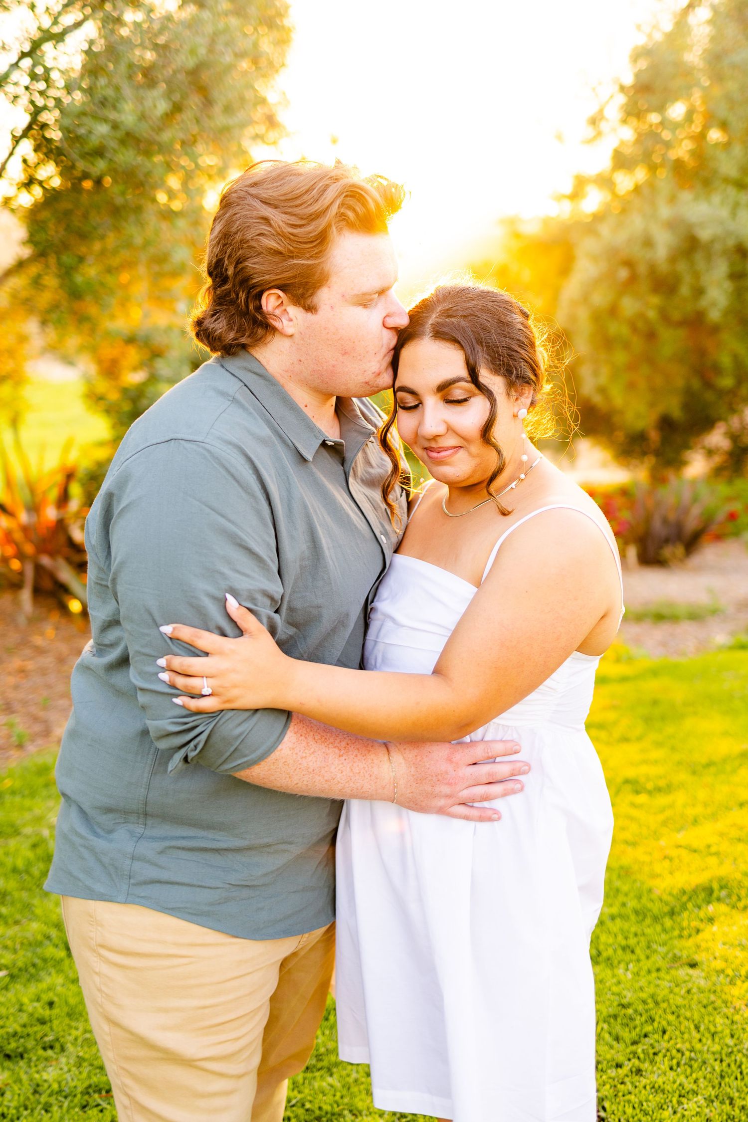 Romantic embrace captured during golden hour with sunlit trees in background.
