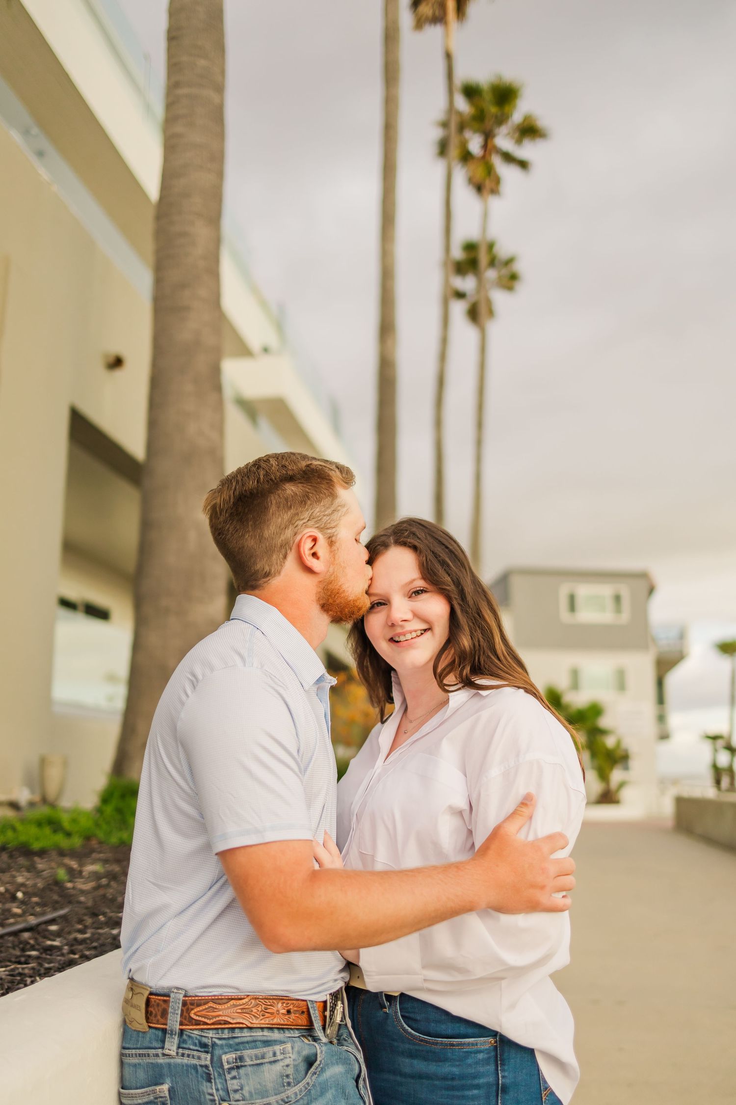 Couple sharing a tender moment and laugh together on urban sidewalk with palm trees.