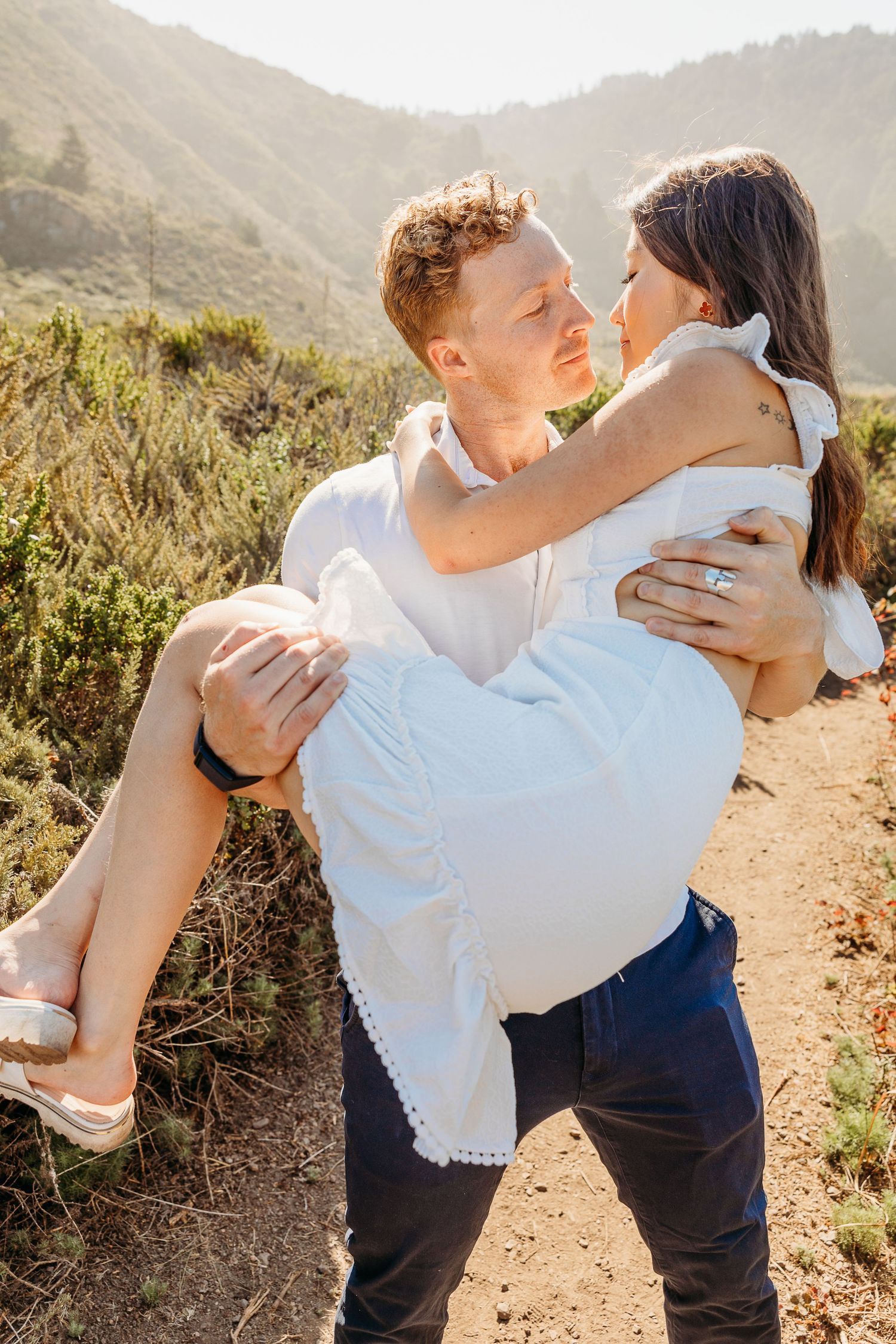 Couple in white clothing share a playful moment on a mountain trail.